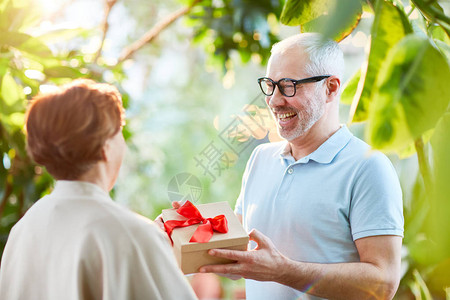 快乐的老人在花园表演时给老婆送盒装礼物庆祝结婚纪念日在花图片