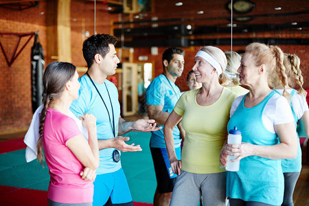 年轻教练在健身房锻炼前向三名老年女团队解释图片