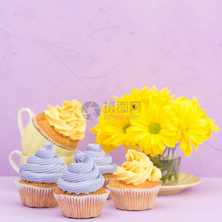 用甜黄色和紫罗兰色奶油和菊花装饰的纸杯蛋糕在紫罗兰色柔和的背景上复制空间区域可用于问候母亲节和情人节卡片图片