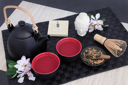 日本genmaichafujiyama茶与东方茶壶杯子拂尘干叶佛像花朵和熏香在黑垫竹背景图片