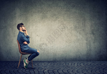 坐在椅子上在灰色背景下考虑计划的孤独的怀念男图片