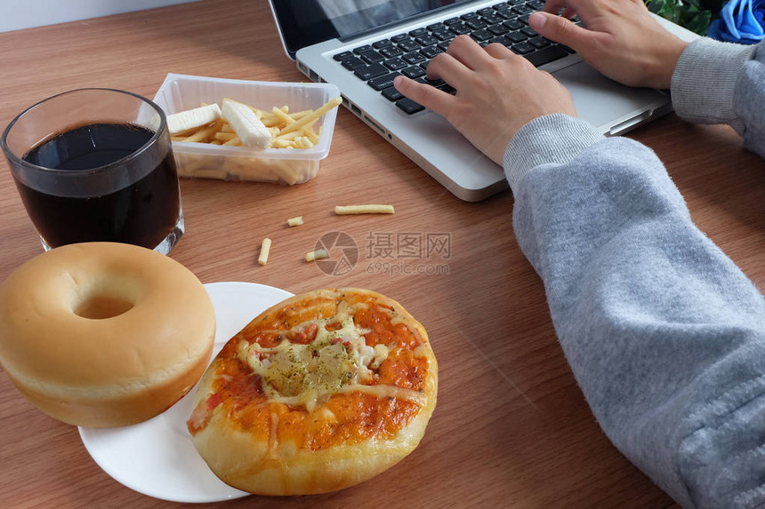 使用笔记本电脑工作期间用甜圈面包披萨和可乐图片