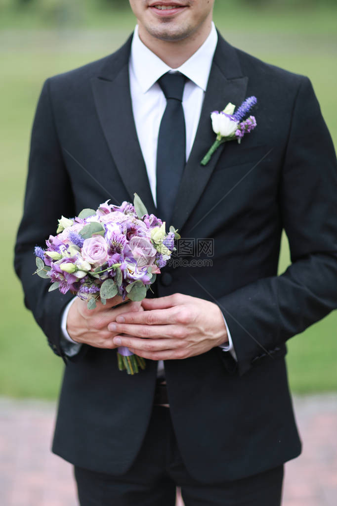 穿着黑色西装和领带的Groom保留着花束图片