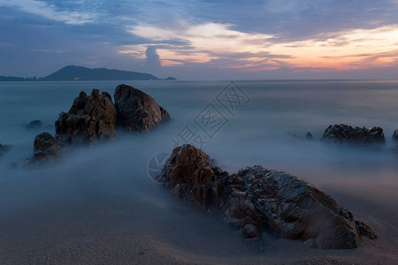 在日落风景背下以岩石绘制的戏剧天空和波浪海景图片