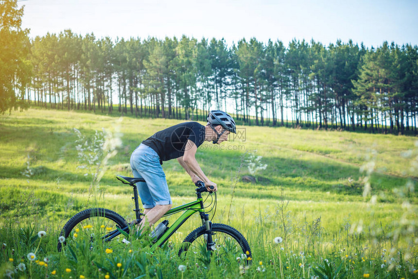 一个戴着头盔的男人在树林间的树林里骑着一辆绿色的山地自行车骑自行车的人在运动积极和健康生图片