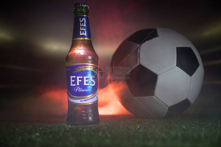 创意概念一瓶EfesPilsner啤酒在草地上与足球和背景模糊的体育场Pilsener是这家公图片