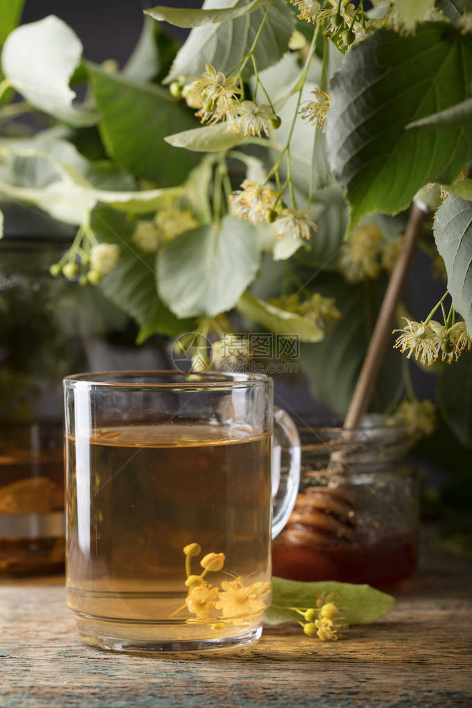 杯椴树茶蜂蜜和木桌上的鲜花图片