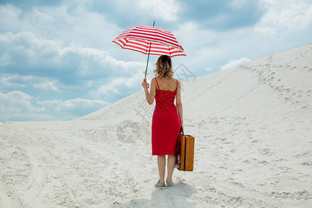 在沙滩上穿红色洋装带雨伞和手提箱图片