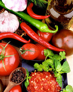 黑碗中的热莎酱配西红柿大蒜辣椒莳萝木勺中的胡椒和木制背景中的橄图片