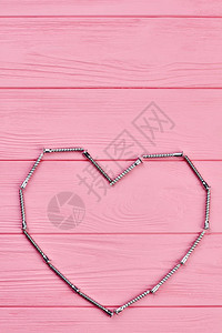 金属紧固件的心形在心形的粉红色木质背景上带有镀锌螺钉的紧固图片