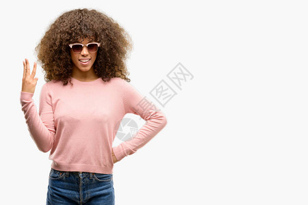 身戴粉红色太阳镜的非洲美妇女展示并举起三指头背景图片