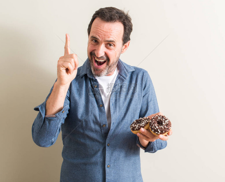 吃巧克力甜圈的老人惊讶于一个想法或问题用快乐的脸对着手图片