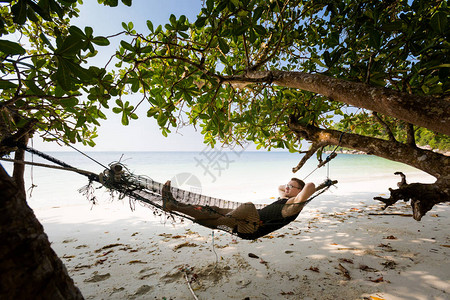 年轻游客在马来西亚邦咯岛秘密海滩上的简单吊床上放松在东南亚采取的美丽图片