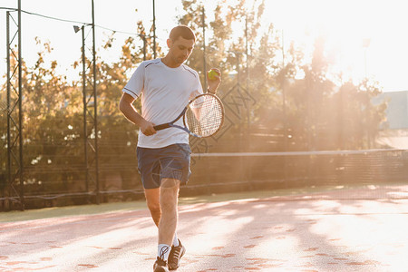 男人早上在阳光下打网球英俊的年轻人在网球场上的照片男子扔网球作为背图片