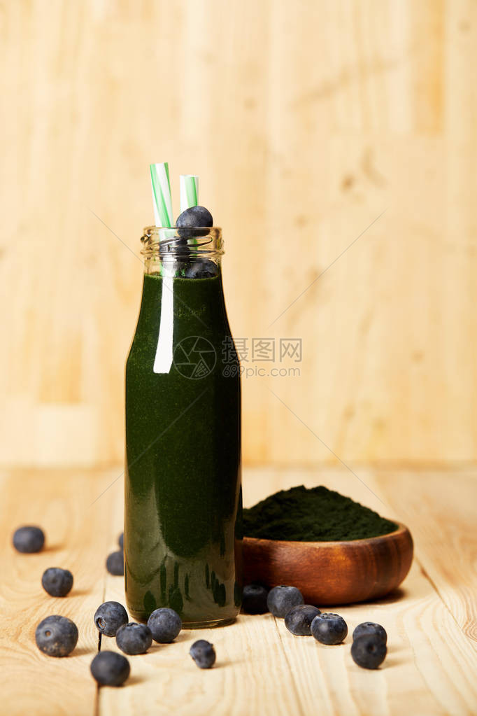 配有碗螺旋藻粉一瓶带有蓝莓和在木制桌上饮用草图片