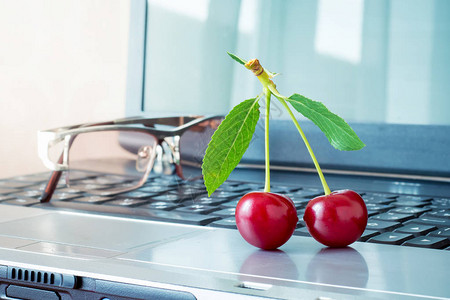 笔记本电脑背景上的红色多汁樱桃在办公时间休息樱桃一种美妙的甜点促进图片
