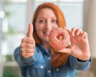 在家拿着甜圈的红发女人开心地笑着做好的手势图片