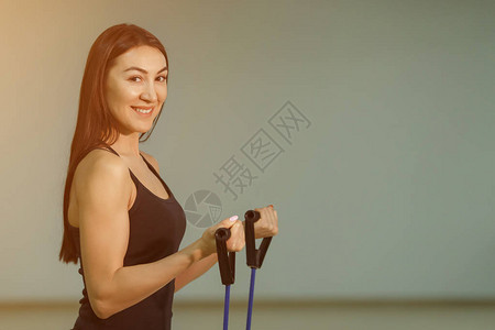 年轻微笑的少女在健身阳光和健身室与扩张器一起做运动图片