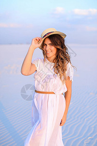身着白礼服和帽子站在沙滩上的年轻女子图片