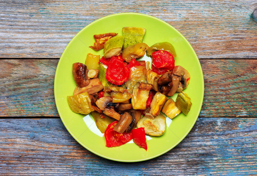 用蘑菇烤的蔬菜和蘑菇冠尼翁放在绿色盘子上在图片