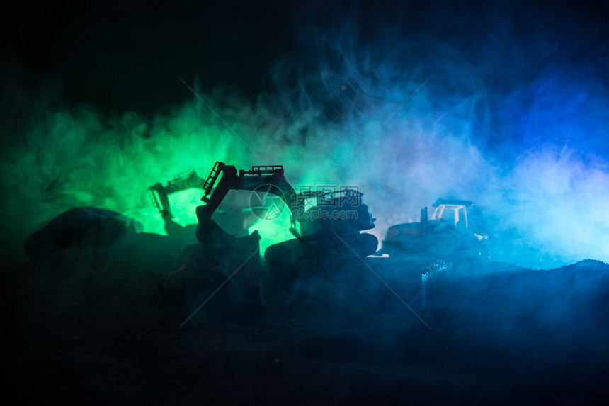 城市街道上的建筑工地夜间停在建筑工地上的黄色挖掘机挖掘机深雾色调背景上的工业概念表装饰图片
