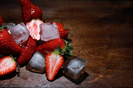 木桌上的新鲜成熟草莓和加水的冰块图片