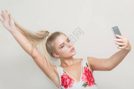 格莱莫金发美女拉头发用手机在灰色背图片