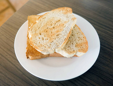 木桌上白盘子里的两片吐司面包图片