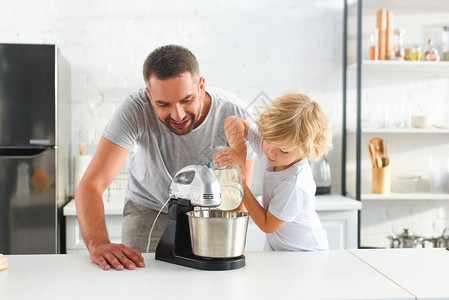 小男孩把面粉倒进搅拌碗里当他父亲站在厨图片
