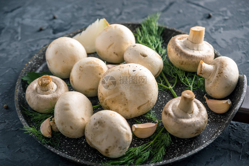 平底锅上的新鲜白色冠军和深色厨房桌子上的配料烹饪蘑菇菜肴图片
