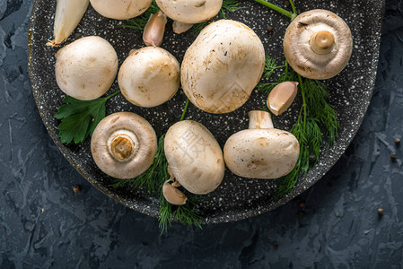 平底锅上的新鲜白色冠军和深色厨房桌子上的配料烹饪蘑菇菜肴图片