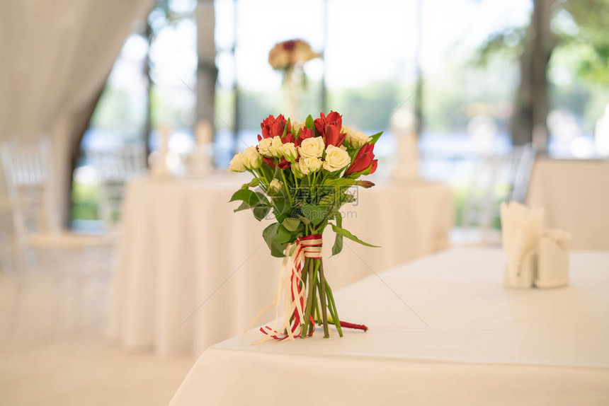 优雅新娘的花束站在桌子上餐桌上有白桌布和空盘子在餐厅图片