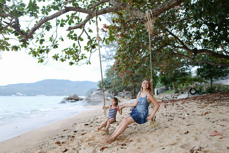 年轻女子与女儿一起在海滩海边和沙滩上摇摆图片