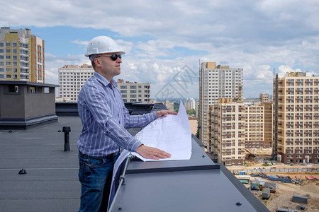 屋顶上有白色头盔和太阳镜的开发工匠或开发商正在查看建筑工地的项目夏图片