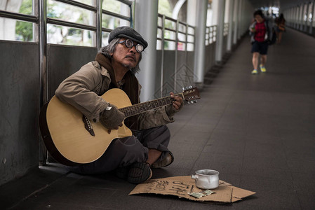 年老的乞丐或无家可归的肮脏男人在现代城市的步行路上唱歌和弹吉他图片