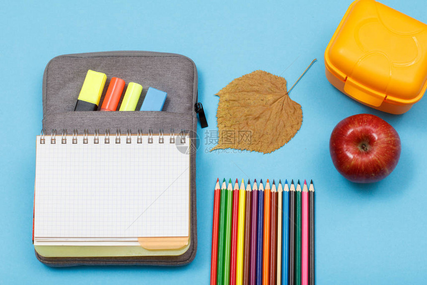 用彩色毡笔和记号笔午餐盒苹果干叶和蓝色背景的彩色铅笔在袋子铅笔盒上打开练习本顶视图回到学校的概图片