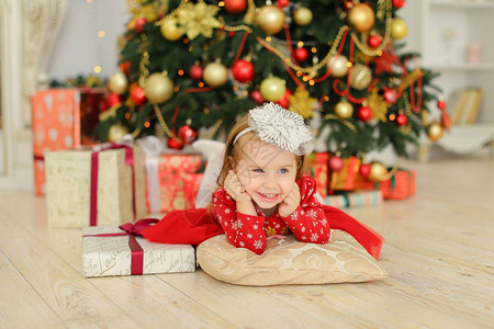 穿着红色连衣裙的金发小女孩躺在圣诞树和礼物附近庆祝寒假儿童图片