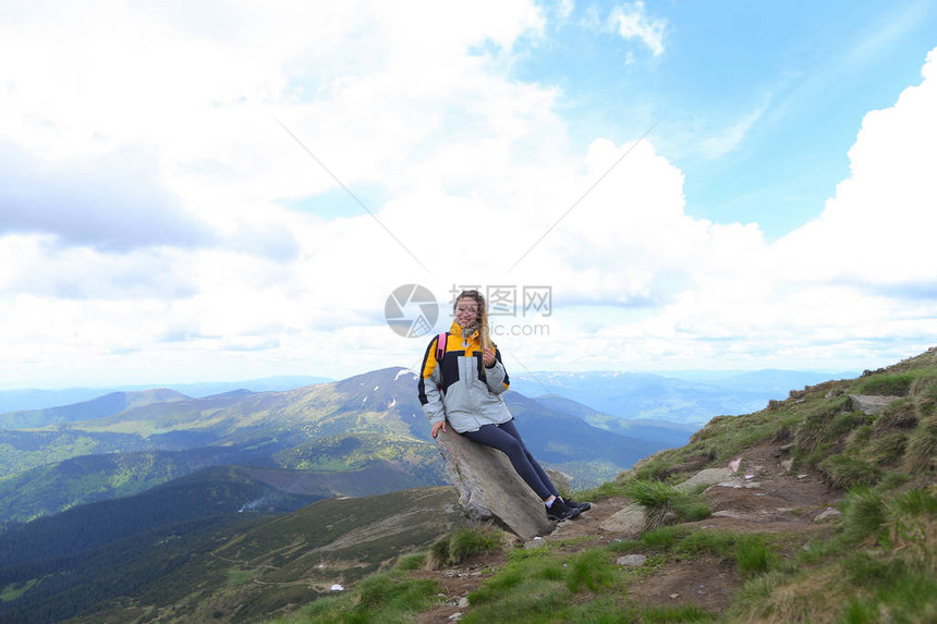 年轻快乐的女游客穿着黄色夹克站在山上图片