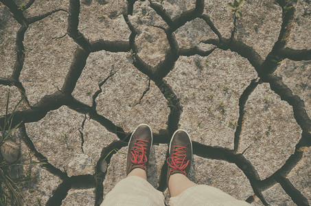 站立在干燥破裂的土壤背景的运动鞋图片