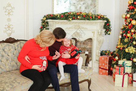 怀孕的白种人妇女与丈夫和女儿坐在圣诞树和装饰壁炉旁幸福家庭和庆图片