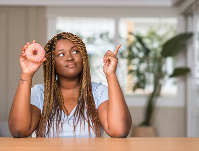 非洲裔美国人吃甜圈的女人惊讶于一个想法或问题用快乐的面孔指图片