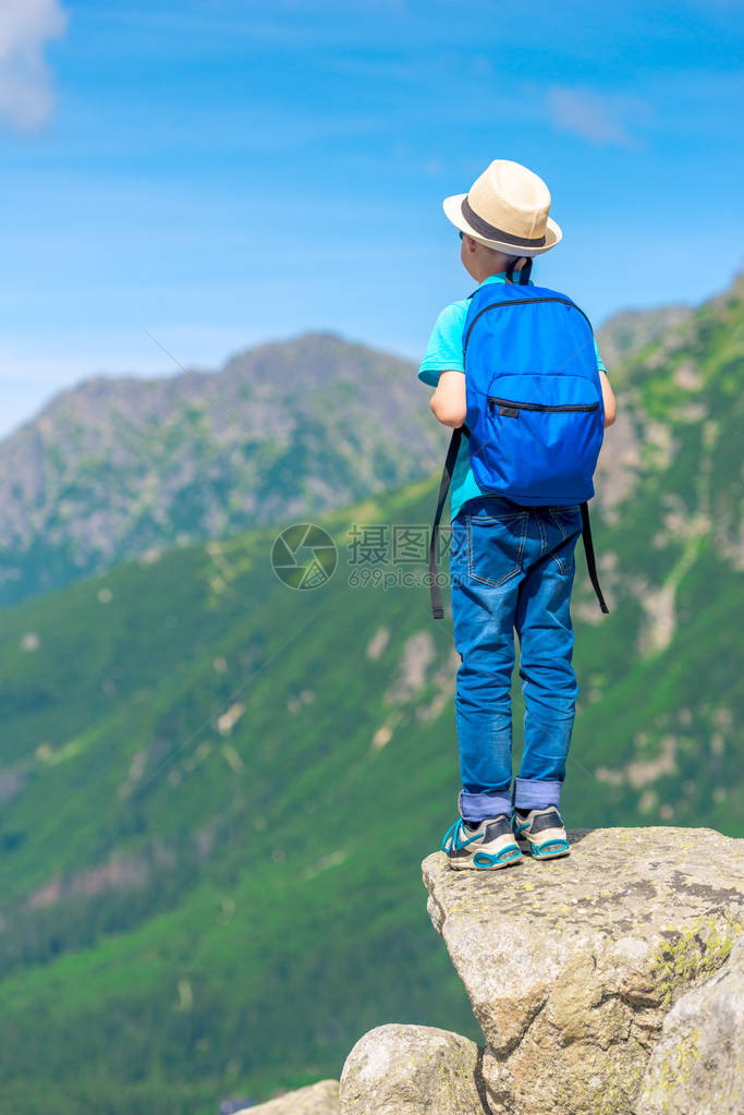从后面的男孩旅行者看背着一个背包站在岩石上享受美丽图片