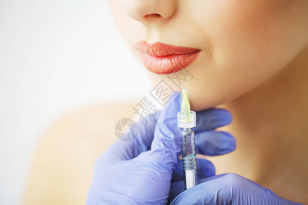 在女嘴唇上注射肉毒杆菌的美容师手的特写她拿着注射器这位年轻美女正在愉图片