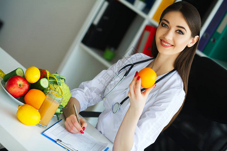健康营养师医生微笑并显示橙色女人手里拿着水果带着美丽的微笑看着橘子上的头皮屑的年轻医背景图片