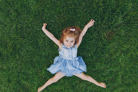 穿着轻便衣服的微笑小可爱小女孩躺在绿草坪上图片