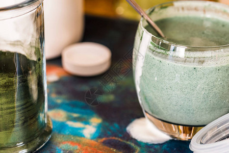 与桌上绿色螺旋藻粉混合的玻璃杯中新鲜Kefirprob图片