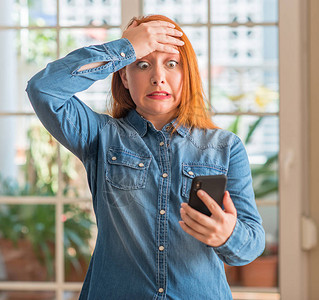 在家里使用智能手机的红发妇女头部压力过大图片