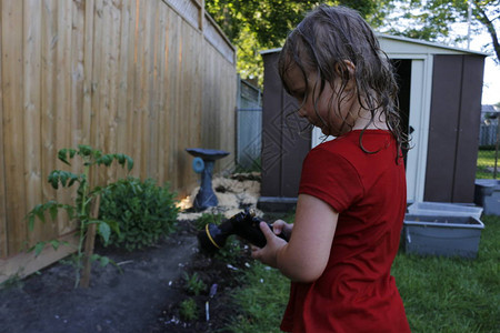 可爱的小孩用水管浇灌后院花园拥图片