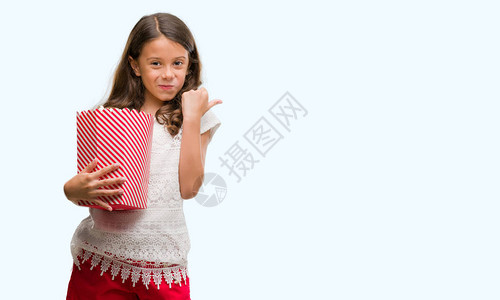 布莱奈特的西班牙女孩吃爆米花指着并用拇指向旁边展示面图片