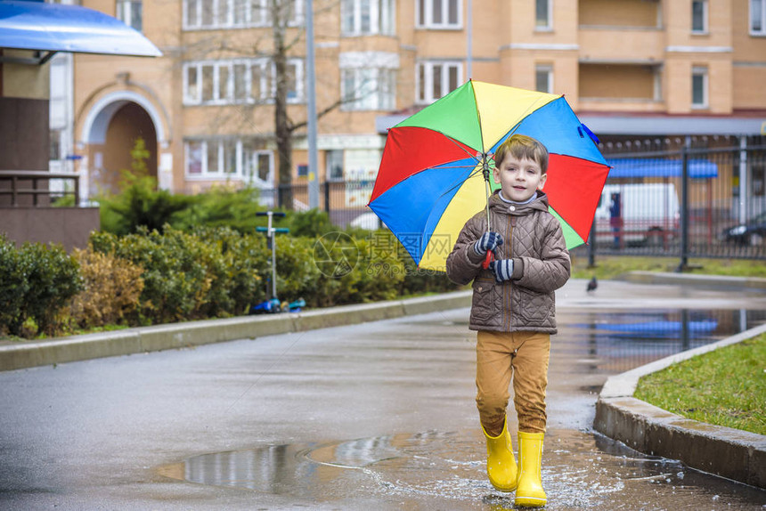 小男孩在多雨的夏日公园玩耍带着五颜六色的彩虹伞防水外套和靴子的孩子在雨中跳进水坑和泥泞中孩子在秋季淋浴间散步任何天气都可以图片